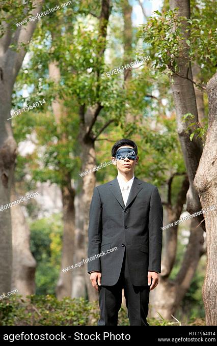 Blindfolded businessman in park with trees