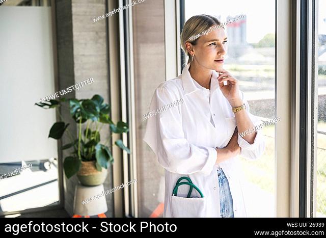 Thoughtful doctor with hand on chin standing by window