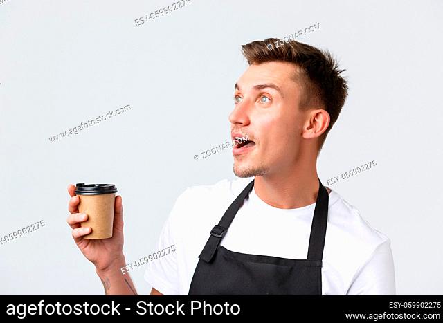 Cafe and restaurants, coffee shop owners and retail concept. Close-up of surprised and amazed blond salesman, barista looking upper left corner and holding...