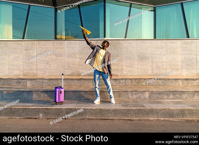 Smiling businessman playing with paper airplane standing on step