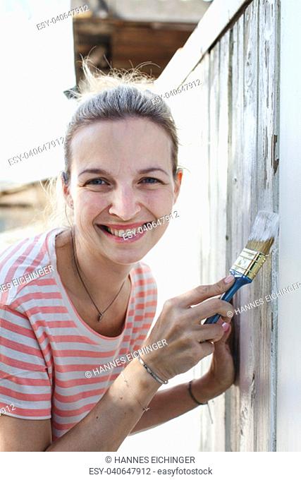 young, pretty woman strokes the garden fence with white paint in summer