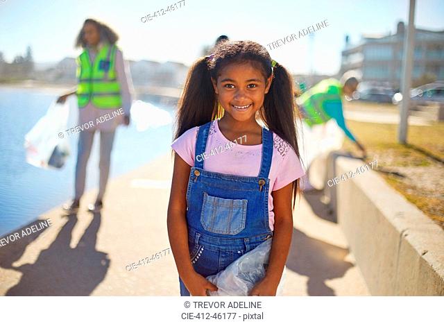 Portrait smiling girl volunteer cleaning up litter on sunny boardwalk