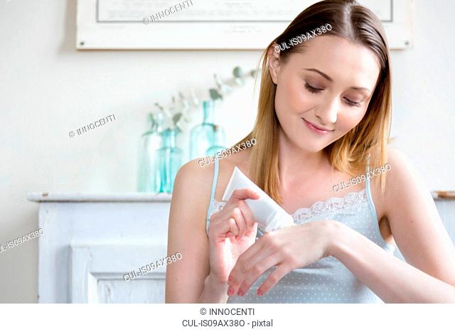 Woman squeezing cosmetic cream onto hand, looking down smiling