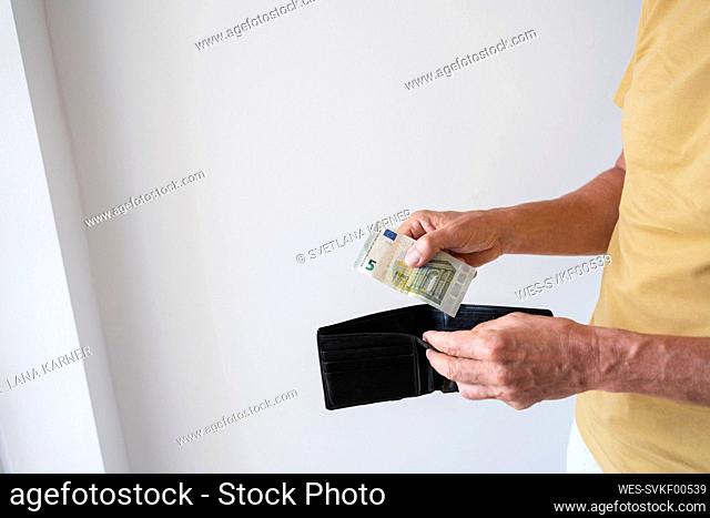 Hands of man holding wallet with banknote standing by wall at home