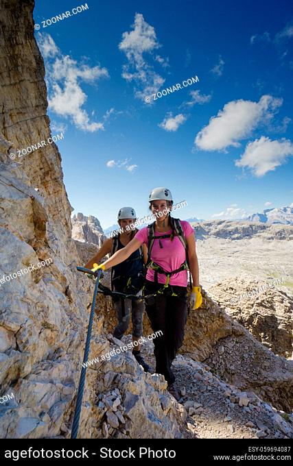 Vertical view of an attractive female climbers and twins on a steep Via Ferrata in the Italian Dolomites with a great view behind