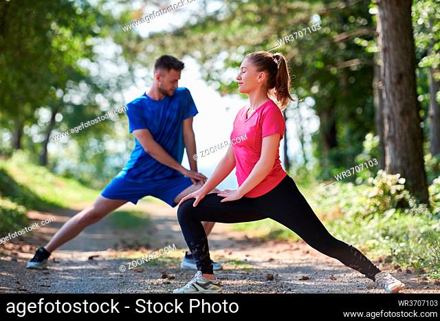 young happy couple enjoying in a healthy lifestyle warming up and stretching before jogging on a country road through the beautiful sunny forest