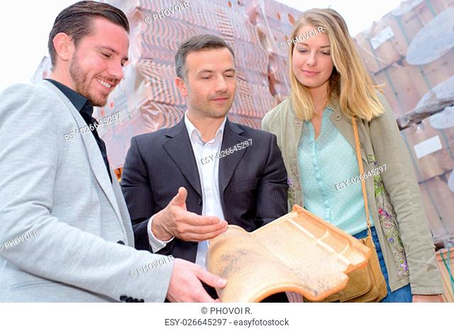 Salesman holding a modern rooftile for couple to see
