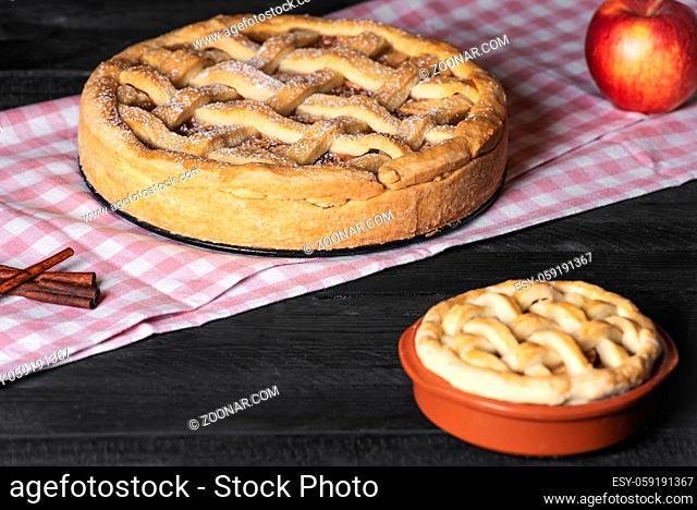 Rustic black table with freshly baked apple pies, with powdered sugar, on a pink towel. Home cooked sweet food. Delicious cakes. National pie day