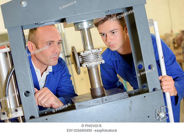 Two men looking at cylinder in vertical vice