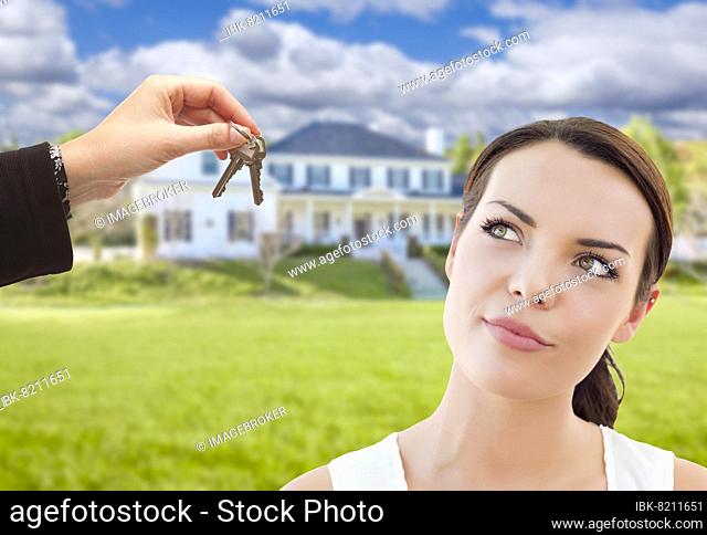 Real estate agent hands thoughtful pretty mixed-race woman keys in front of house