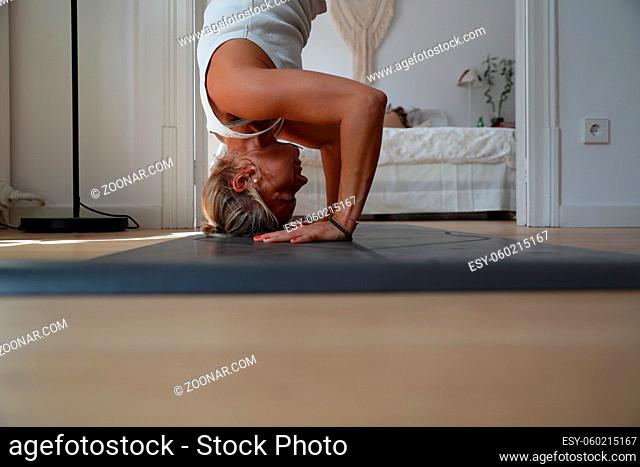 Woman practicing yoga, working out, wearing white t-shirt, pants, meditation session at floor window with city view. Full length. High quality photo