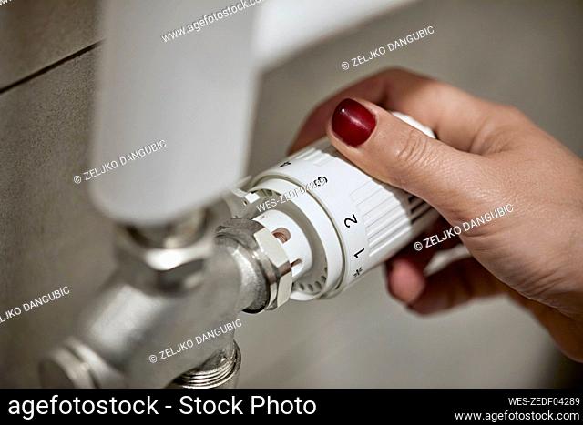 Woman adjusting thermostatic radiator valve of heating boiler at home