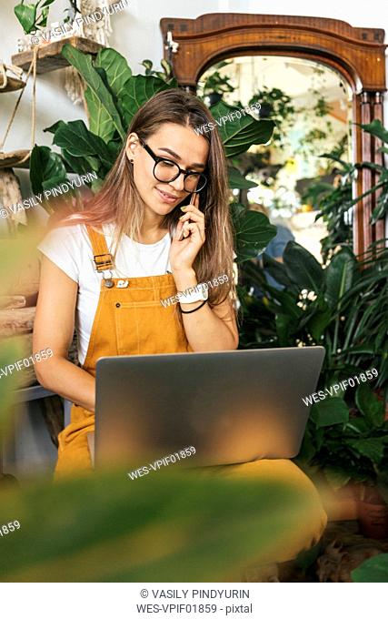 Young woman with laptop on the phone in a small gardening shop