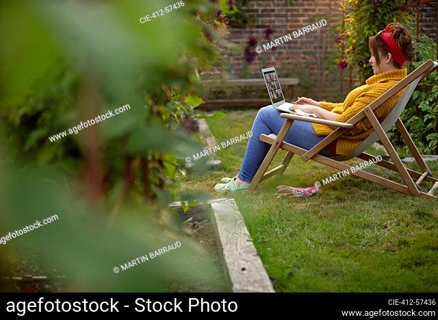 Woman working at laptop in lawn chair in summer garden