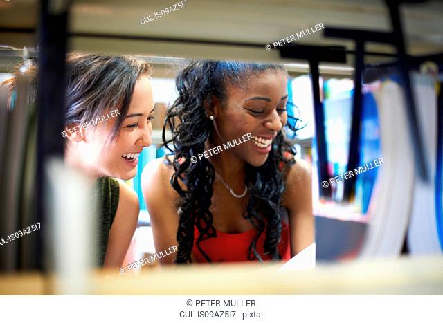 Two young female college students looking on library shelves