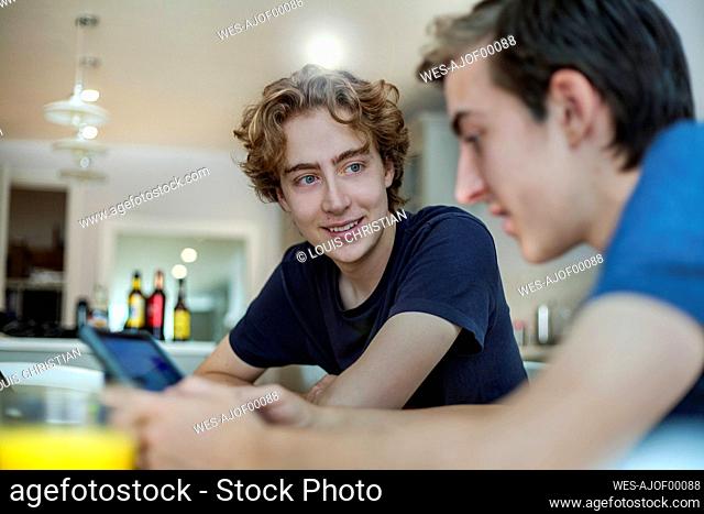 Smiling young man looking at friend using smartphone at home