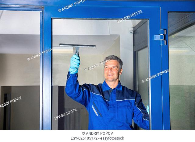 Happy mature male worker cleaning glass with squeegee
