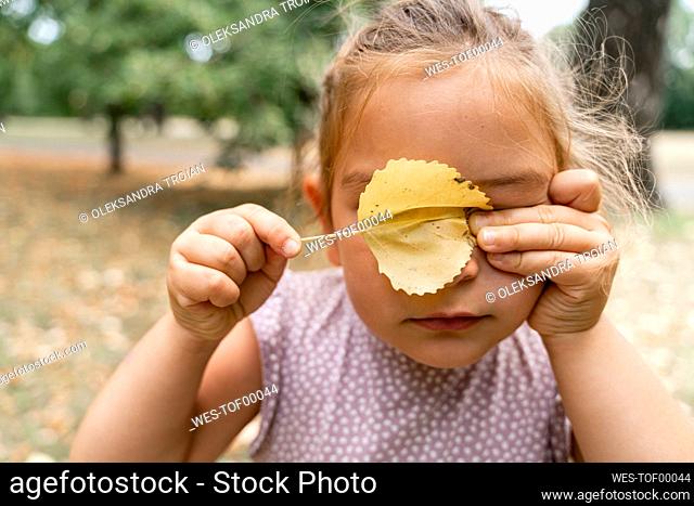 Girl covering eyes with leaf at public park