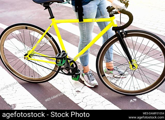 Delivery woman with bicycle standing on zebra crossing