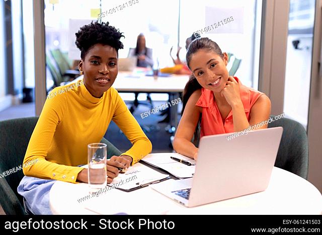 Portrait of happy young female advisors sitting with laptop at desk in modern workplace