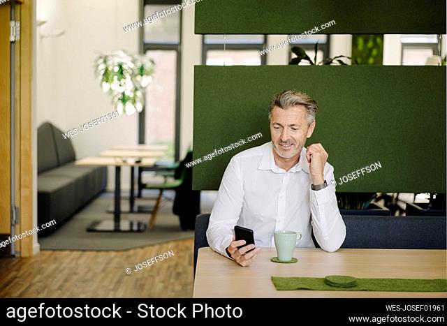Smiling businessman using mobile phone while sitting on table at cafeteria
