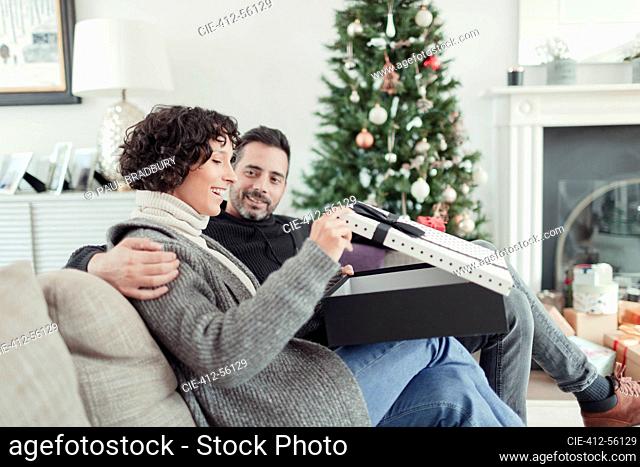 Woman opening Christmas gift from husband on living room sofa
