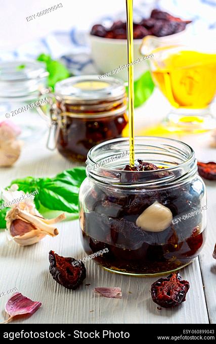 Pour olive oil over the spicy dried plums with Italian herbs in glass jars. Concept of preparing home-made products that are resistant to storage