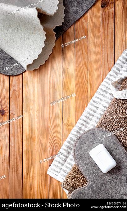 Accessories for visiting the bath or sauna on a wooden background: towel, bath mat, felt hat, washcloth, soap. Top view with copy space. Flat lay