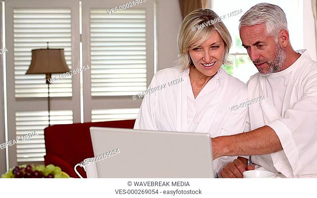 Happy couple using laptop together in bathrobes