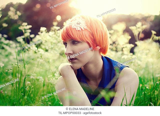 Young girl with orange hair and blue top looking away, in a field of flowers, with sunset light