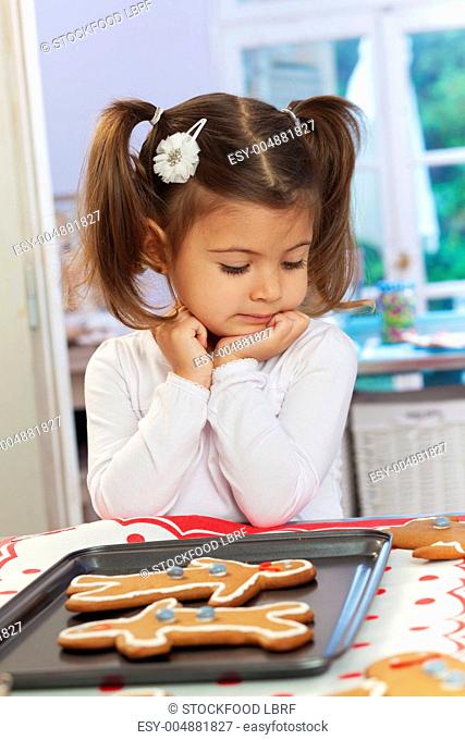 A little girl in front of a baking tray of gingerbread men
