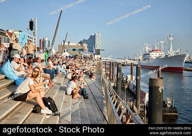 10 September 2023, Hamburg: Numerous people enjoy the evening sun on the Jan Fedder Promenade at the harbor. In the background, the Elbphilharmonie