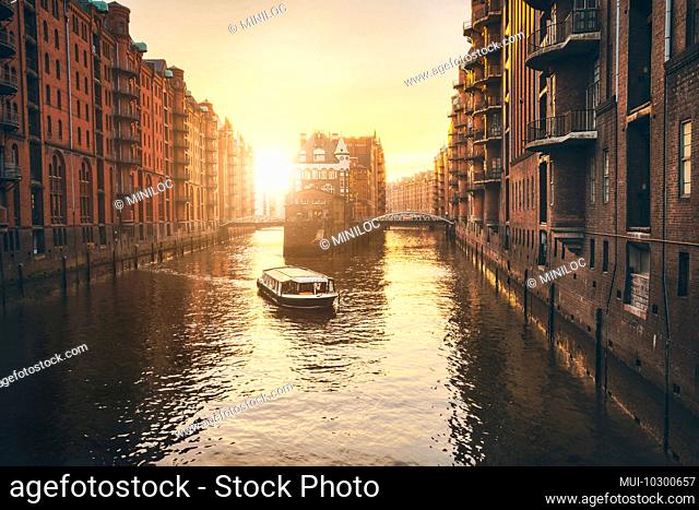 Hamburg warehouse district in golgen hour sunset lit. Water castle palace and tourist visting boat trip in river. Old warehouse port, Germany, Europe