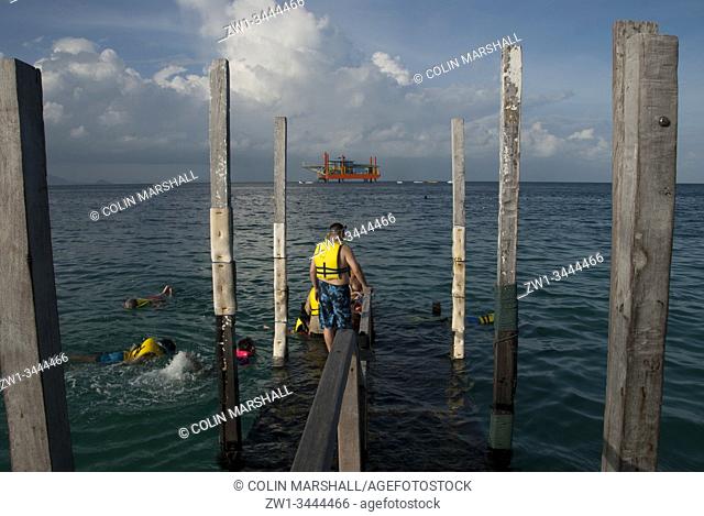 Man on jetty wearing life jacket about to get into water to join other snorkellers with oil rig in background, Sipadan Water Village, Mabul Island, Sabah