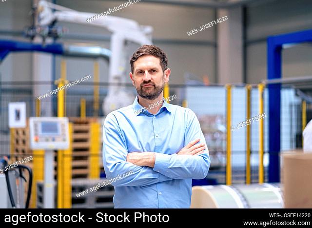 Businessman with arms crossed standing in front of machinery at industry