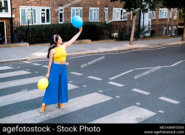 Woman with hand raised holding balloons standing on zebra crossing