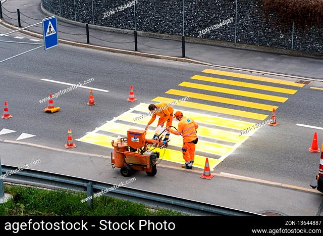 Maienfeld, GR / Switzerland - April 2, 2019: workers painting and marking a pedestrian crosswalk with fresh yellow paint to ensure road and pedestrian safety