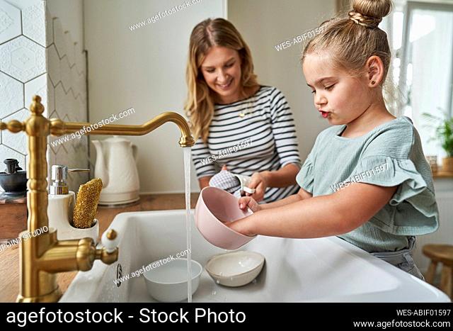 Girl washing bowl with mother in kitchen at home