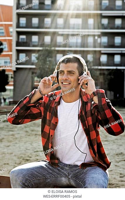 Smiling young man sitting outdoors in the city wearing headphones