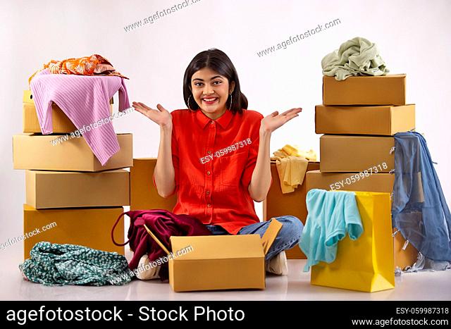 A young woman sitting amidst boxes, clothes and shoppingbags overjoyed on unpacking new dress