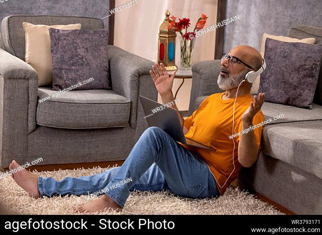 Senior man listening music through headphones while sitting on floor in living room