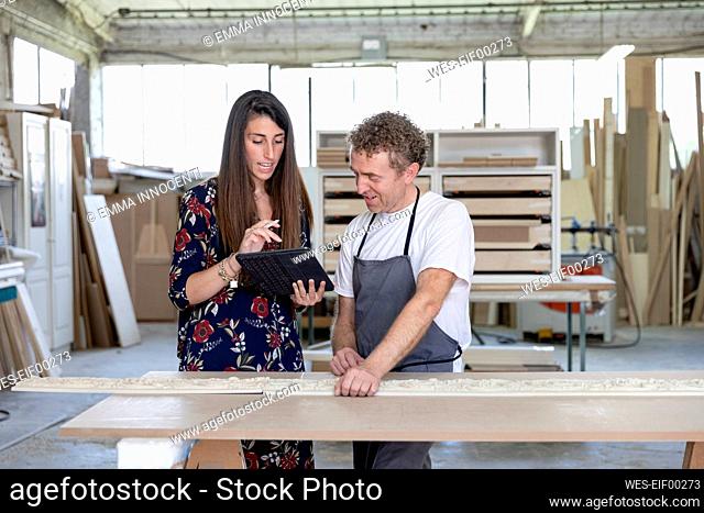 Interior designer showing digital tablet to carpenter while standing at workshop
