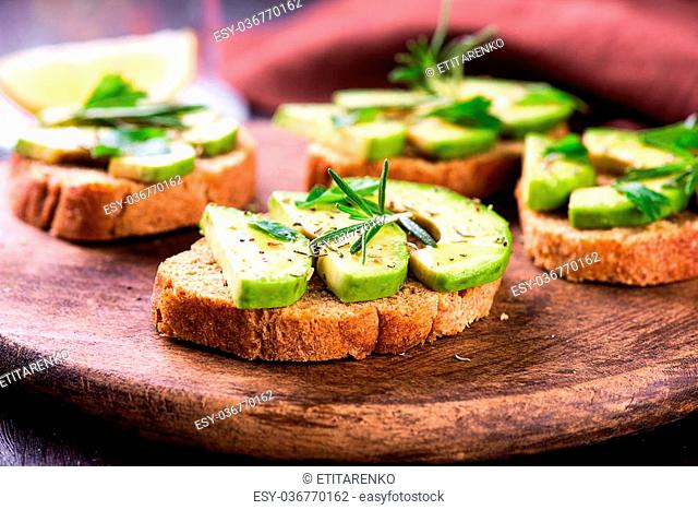 Toast with rye bread and avocado, herbs on wooden board