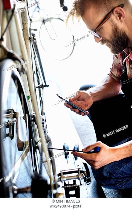 A bike mechanic in a bicycle repair shop using a smart phone