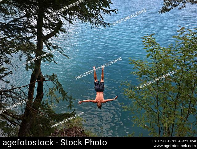 15 August 2023, Bavaria, Schwangau: A young man jumps from the steep bank into the turquoise water of the Alpsee. It is supposed to remain midsummery: Also for...