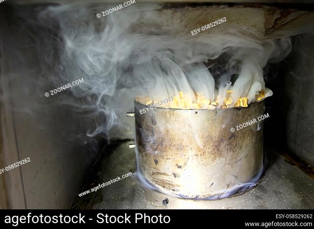Metal pot with sawdust and smoke in an industrial oven for smoking fish