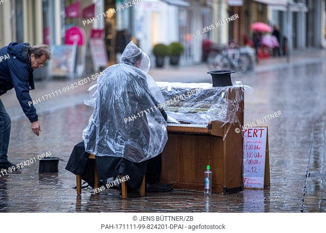 A street musician playing his piano under the pouring rain on the main shopping street of Schwerin, Germany, 11 November 2017