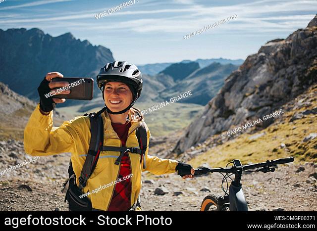 Ciclista femenina sonriente tomando selfie con bicicleta de montaña contra la montaña, el Parque Nacional de Picos de Europa, Cantabria, ESPAÑA