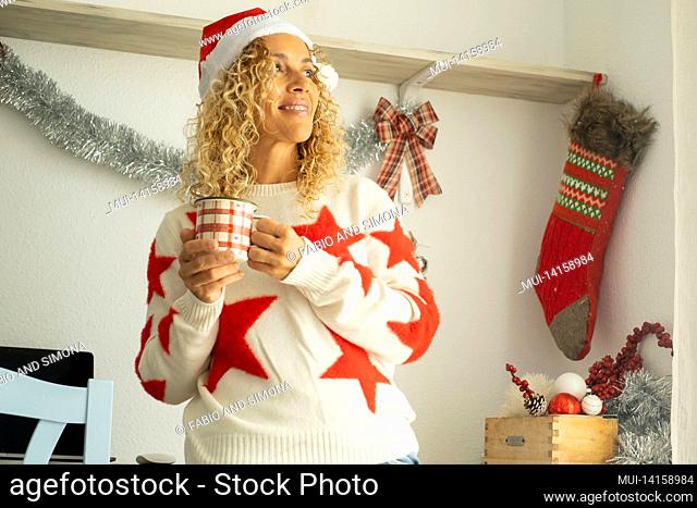 happy and pleasent woman smile and enjoy christmas celebration and decoration at home alone drinking tea and wearing santa claus hat - happy people celebrate...