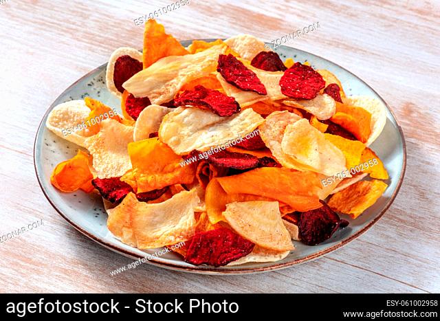 Vegetable chips on a plate, a healthy vegan snack on a wooden background